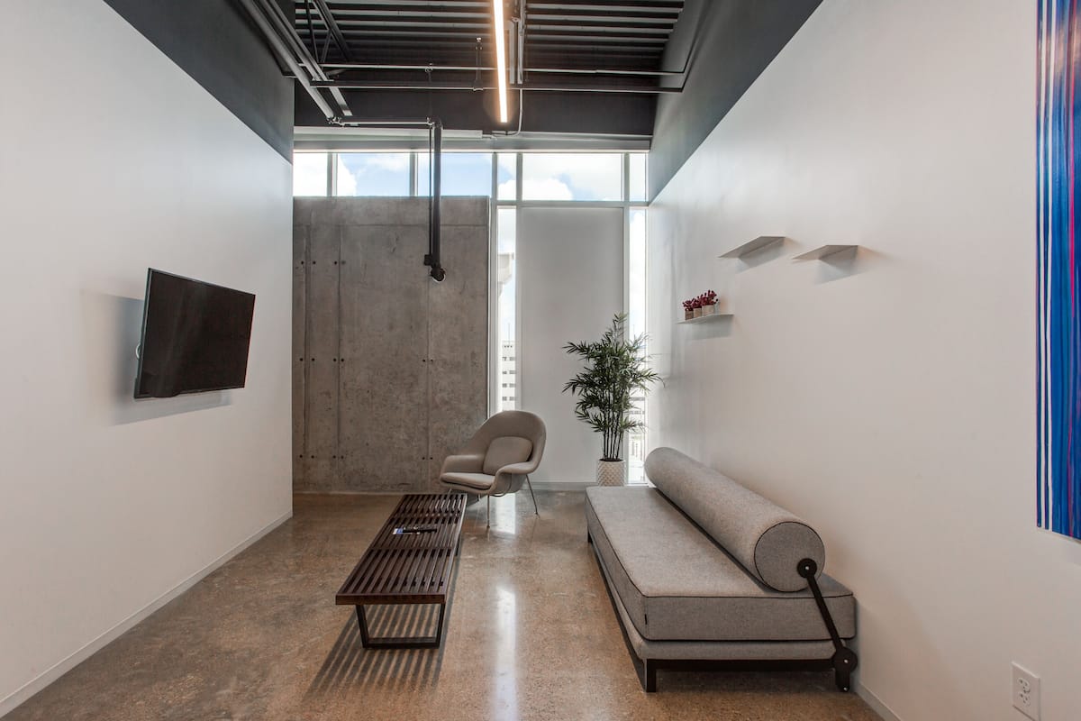 A modern interior with a concrete wall, a flat-screen TV, a sofa, a chair, and a potted plant.