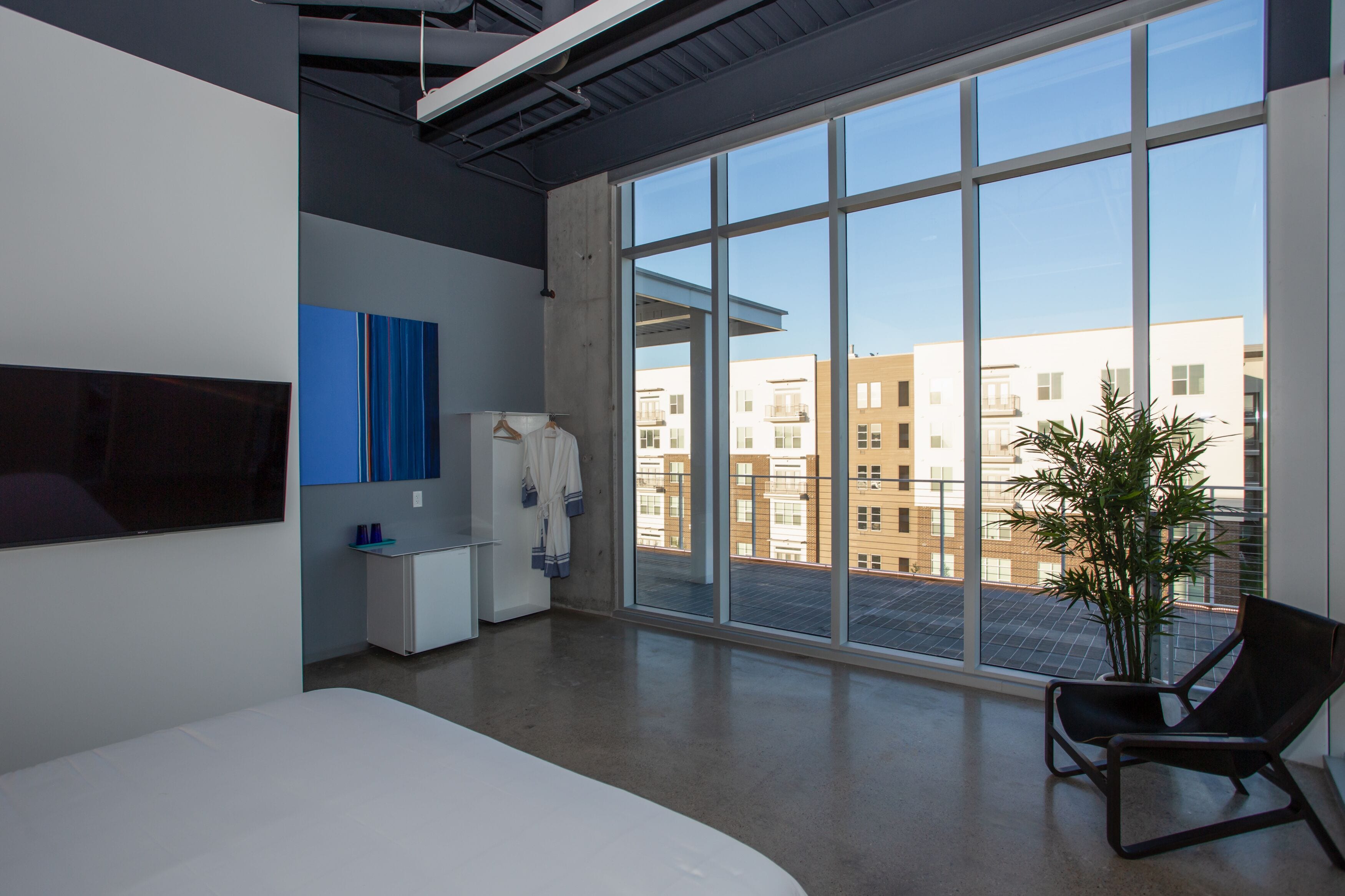 A modern hotel room with a large window, a bed, a desk, and a chair.