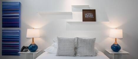 A hotel room with a bed, two bedside tables, two lamps, a phone, and a 'HOTEL REVEL' sign on the wall.