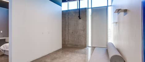 Une pièce moderne et minimaliste, avec un mur d’accent en béton, un banc intégré et une grande fenêtre qui laisse entrer la lumière naturelle.