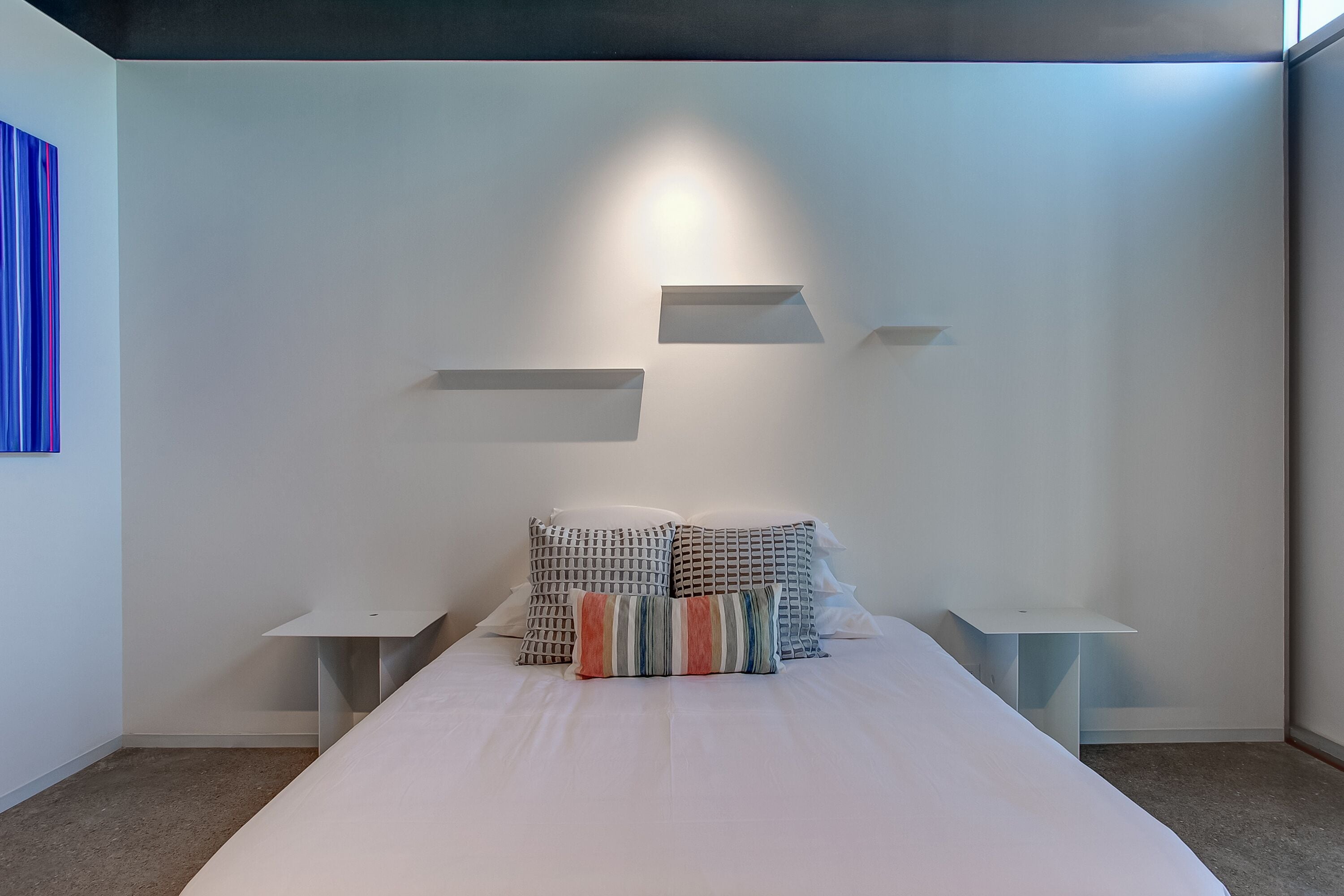 Un dormitorio moderno con una cama grande, dos mesitas de noche y un estante en la pared.