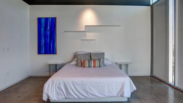 A modern bedroom with a large bed, a blue abstract painting, and a minimalist design.