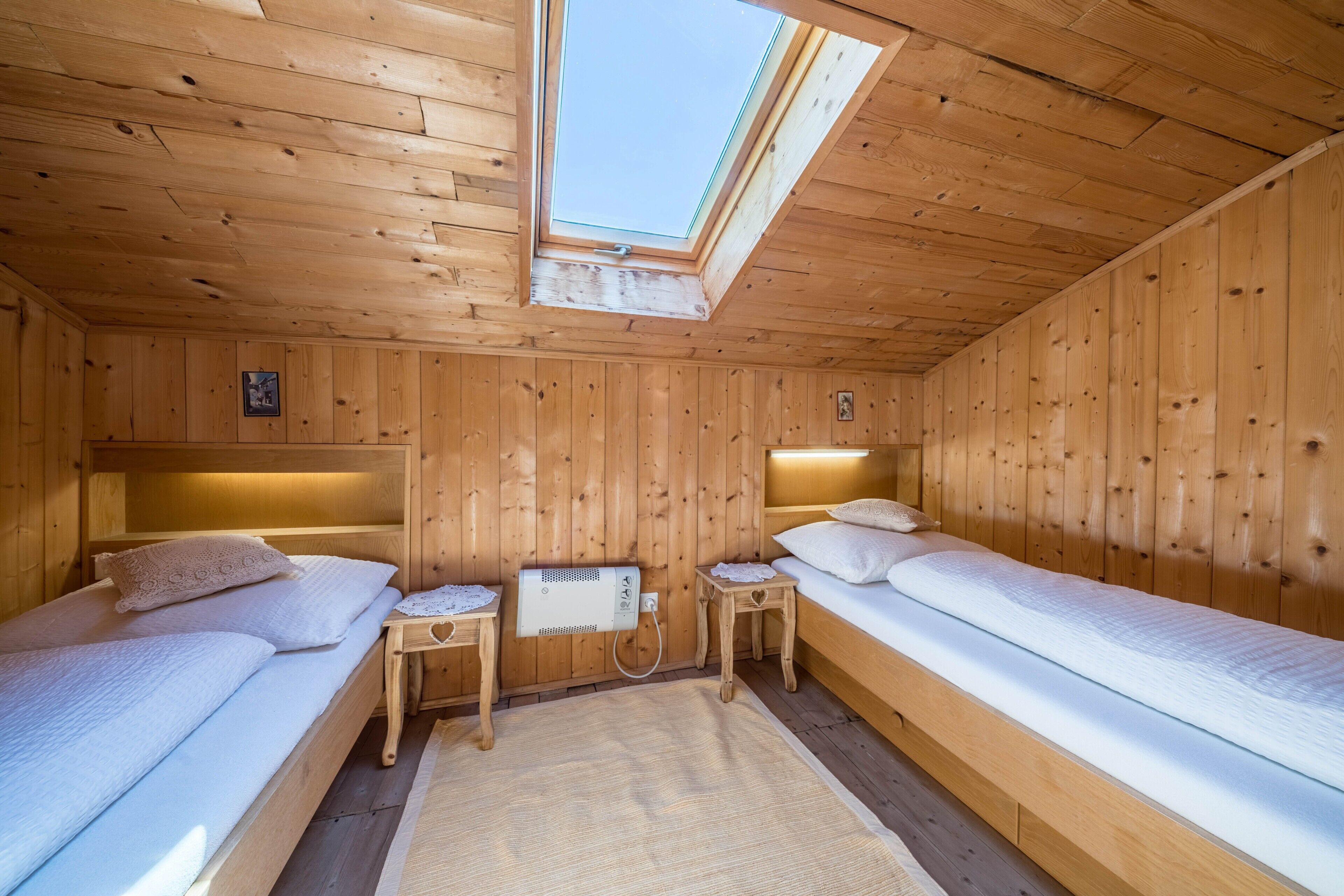 A wooden cabin room with two beds, a skylight, and a small table with a heater.