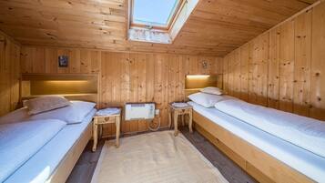 A wooden cabin room with two beds, a skylight, and a small table with a heater.