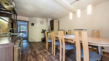 Une cuisine moderne dotée d’une hotte en acier inoxydable, d’une table à manger en bois avec des chaises, et offrant une vue sur l’extérieur par la porte.