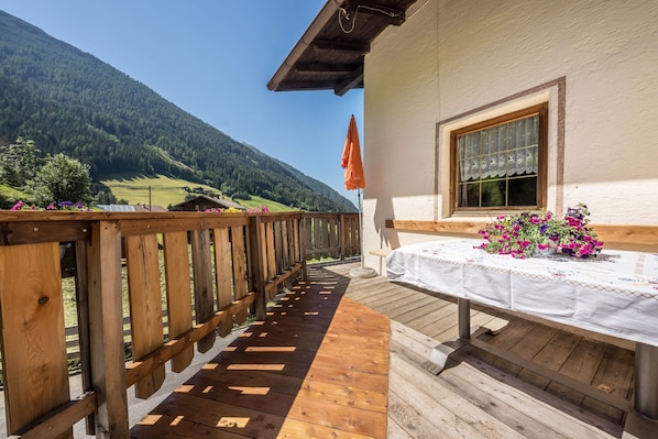 A wooden deck with a table and flowers, overlooking a mountainous landscape. - Beautiful Holiday Home “Ferienhaus in der Blaiche”  with Mountain View, Wi-Fi, Balcony, Garden. (St.Leonhard Passeier)
