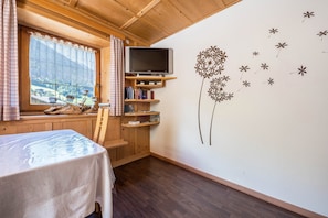 A wooden cabin room with a table, bookshelves, a TV, and a window with curtains. - Beautiful Holiday Home “Ferienhaus in der Blaiche”  with Mountain View, Wi-Fi, Balcony, Garden. (St.Leonhard Passeier)