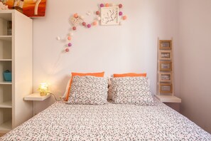 A bedroom with a bed, two pillows, a nightstand with a lamp, a wall-mounted shelf, and a decorative string of balls. - Central Apartment "Miguel Benitez" On the Beach with Terrace, Ocean View & Wi-Fi (El Cotillo)