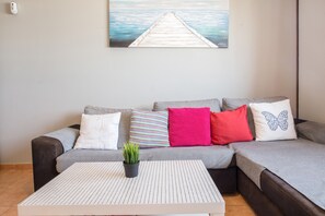 Ein Wohnzimmer mit einer Couch, Kissen, einem Couchtisch und einem Gemälde von einem Pier.