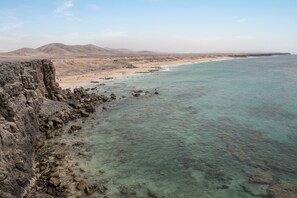 Eine Küstenlandschaft mit felsigen Klippen, einem Sandstrand und klarem türkisblauem Wasser.