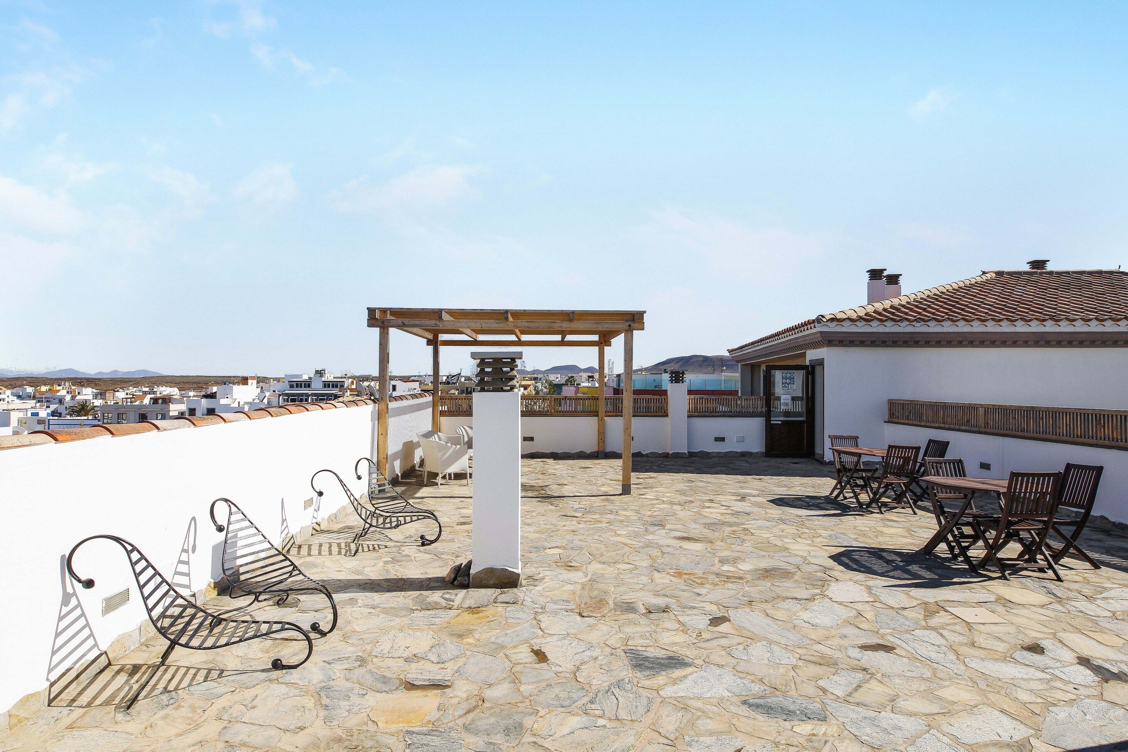A rooftop terrace with stone flooring, a pergola, outdoor seating, and a view of the cityscape.