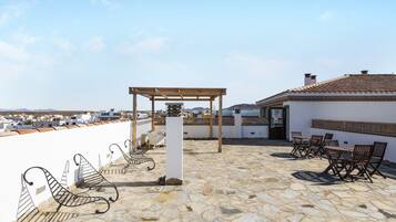 A rooftop terrace with stone flooring, a pergola, outdoor seating, and a view of the cityscape.