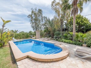 Una piscina con cubierta de piedra, rodeada de plantas y árboles tropicales.