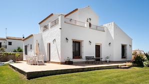 A two-story white house with a balcony, a patio with outdoor furniture, and a well-maintained lawn. - In a quiet location with sea view - El Mirador de Castilnovo (El Palmar (Cádiz))