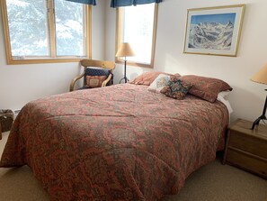 A bedroom with a large bed, a chair, a lamp, and a painting on the wall.