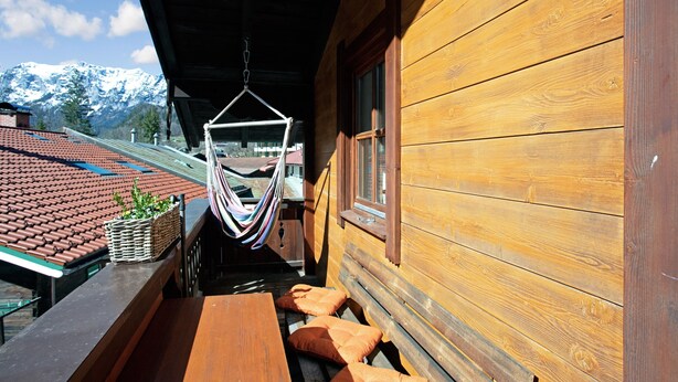 Eine Holzhütte mit einer Hängematte, einer Holzbank und Blick auf einen Berg.