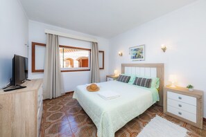 Un dormitori amb llit, taules de nit, televisió, finestra amb cortines i un paviment amb dibuixos.