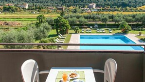 A balcony with a table, two chairs, a pool, and a view of a green landscape with houses and trees.