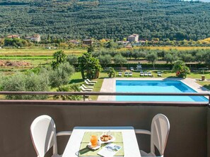 Un balcon avec une table, deux chaises, une piscine et une vue sur un paysage verdoyant, avec des maisons et des arbres.
