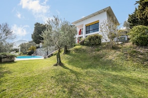 A modern house with a swimming pool, surrounded by greenery and trees.