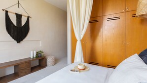 A bedroom with a bed, a wooden wardrobe, a bench, and a macramé wall hanging.