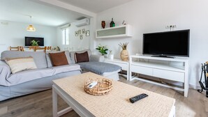 Una sala de estar moderna con un sofá, televisor y una mesita consola blanca.