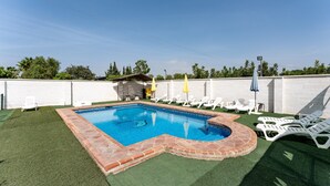 Un patio trasero con piscina, césped artificial y sillas de lounge blancas.