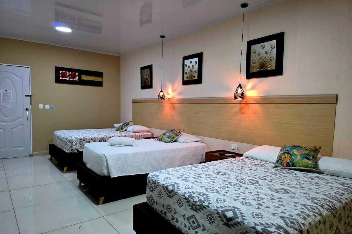 A hotel room with three beds, a wooden headboard, and wall-mounted artwork.