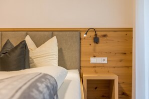 Un letto con cuscini, un comodino, una lampada a parete e una presa elettrica.