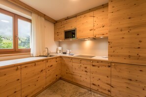 Cucina con mobili in legno, forno a microonde integrato, finestra con tende e pavimento in pietra.