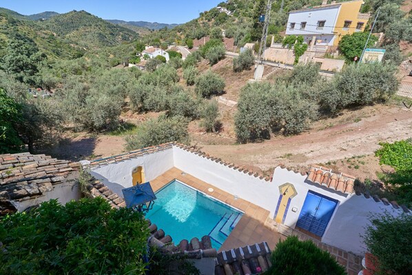 A pool with a blue door, surrounded by a white building with terracotta roof tiles, set in a hilly landscape with olive trees. - Holiday Home Villa Carlitos with Mountain View, Balcony, Terrace (Comares)