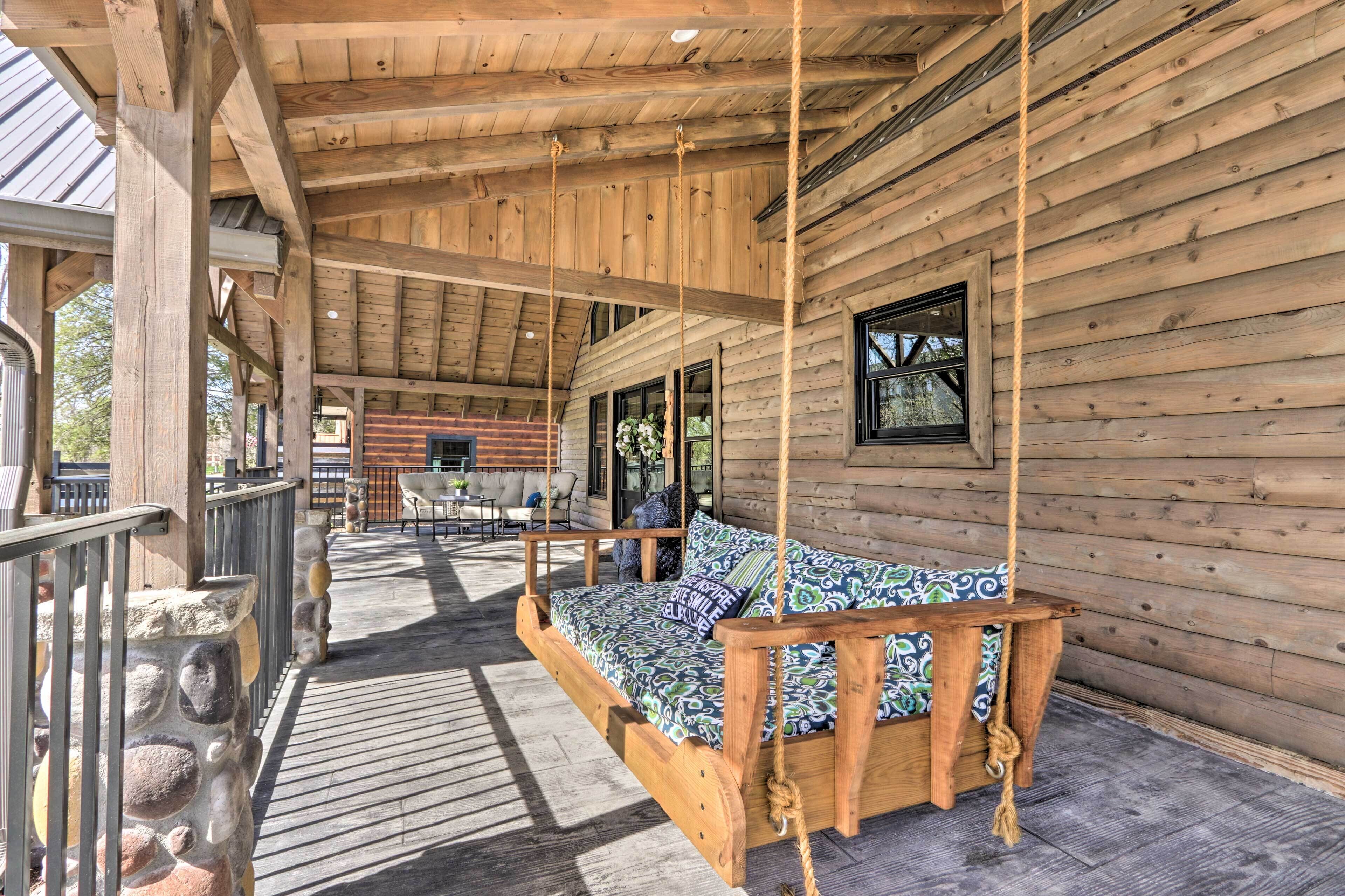 Une cabane en bois avec une véranda, un lit suspendu et un mur en pierre.