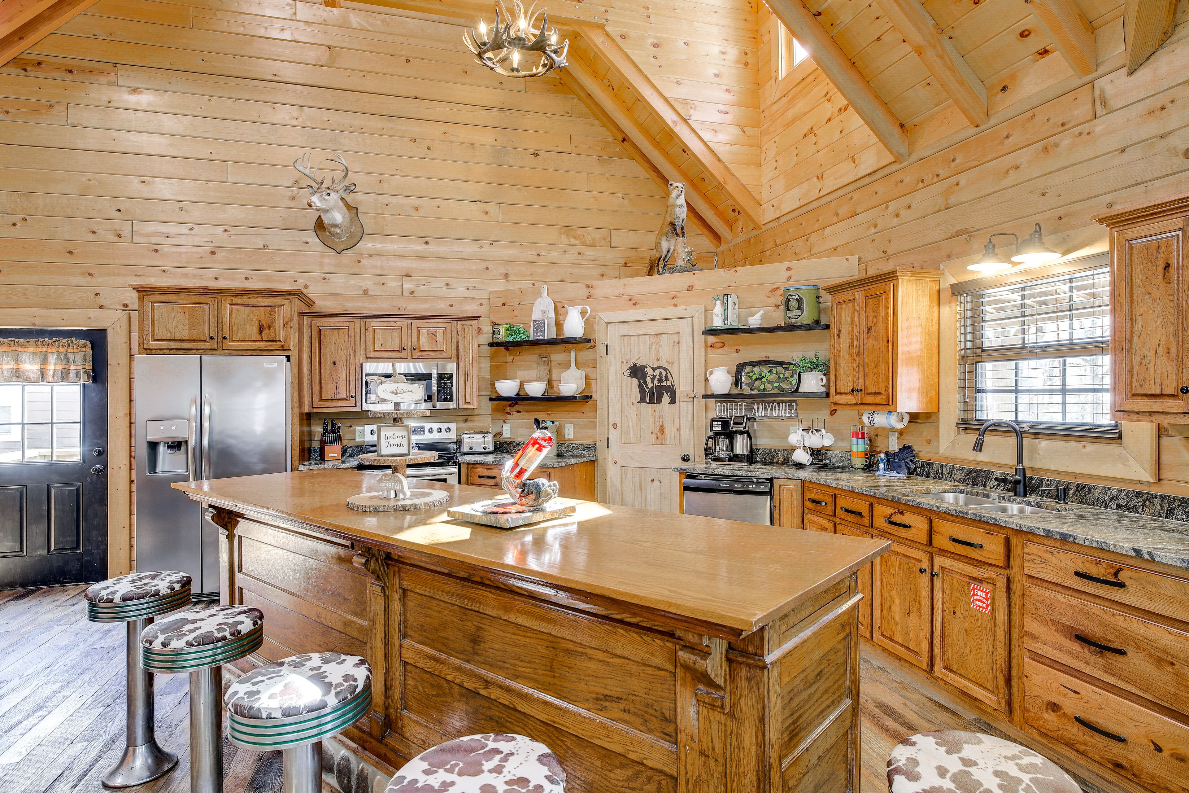 A wooden cabin kitchen with a large island, bar stools, and a mounted deer head.