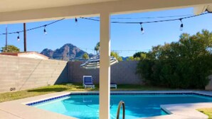 A backyard with a swimming pool, a patio with a table and chairs, and a view of a mountain. - Uptown remodeled home and heated pool (Phoenix)