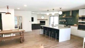 A modern kitchen with a central island, bar stools, and a dining area with a wooden table and chairs. - Uptown remodeled home and heated pool (Phoenix)