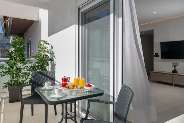 A balcony with a table set for breakfast, including a coffee cup, croissants, and a fruit bowl.