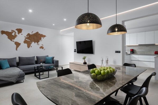 A modern living room with a large dining table, grey sofas, and a world map on the wall.