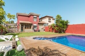 A residential property with a swimming pool, a wooden deck, and a red wall.