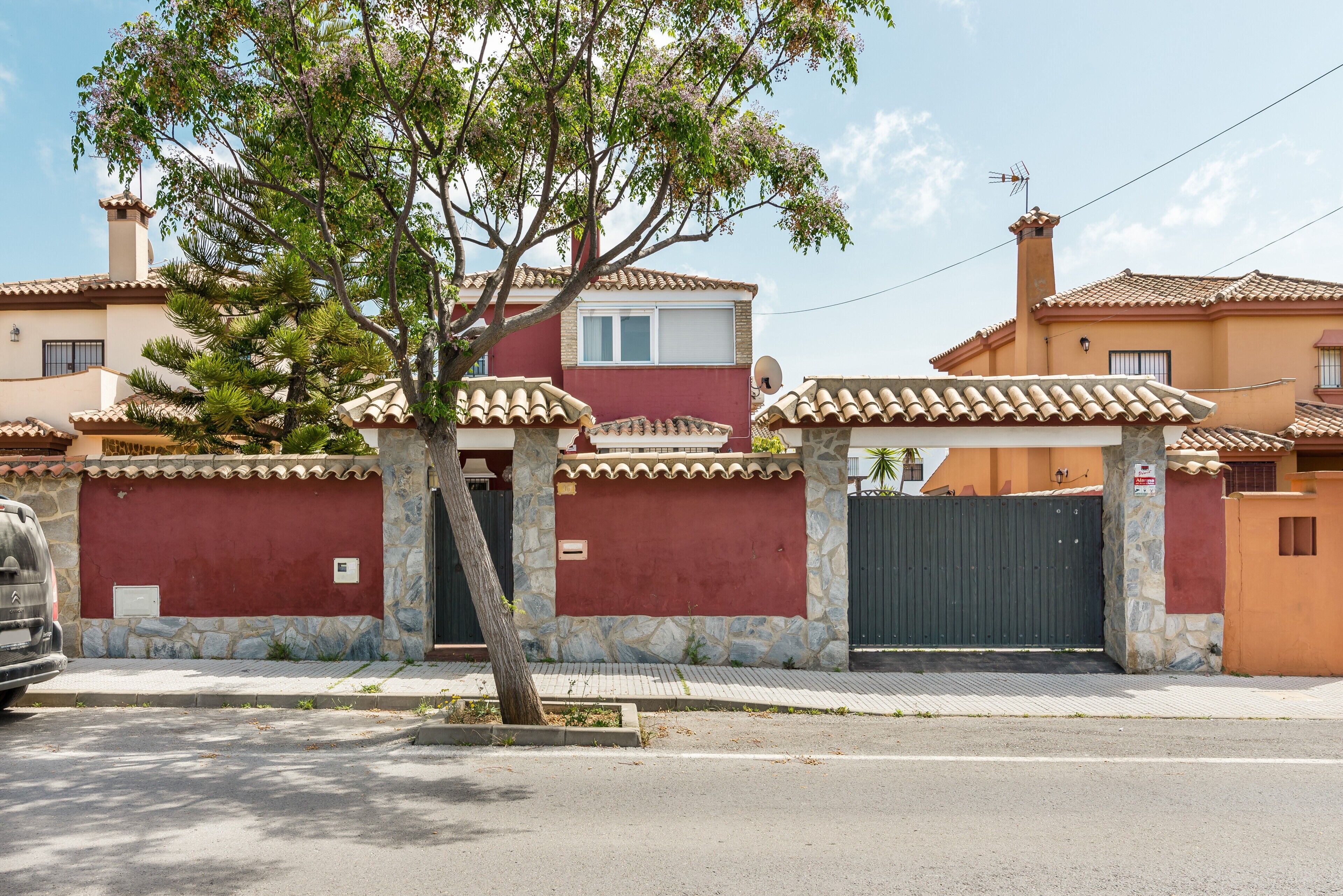 Una zona residencial con entrada vigilada, muros de piedra y techos de tejas.