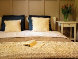 Ein Bett mit einem Buch, zwei Kissen und einer Vase mit Blumen auf einem Nachttisch.