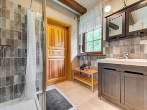Ein Badezimmer mit Dusche, einer Holztür, einem Fenster und einem Waschbecken mit Spiegel.