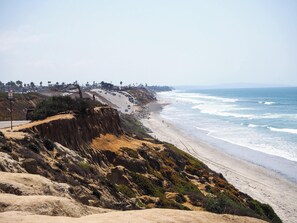 A coastal road with a beach on the right, a rocky cliff on the left, and a clear sky. - Gorgeous Newly Renovated Carlsbad Beach Home (Carlsbad)