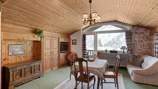 A cozy room with wooden walls, a stone fireplace, a dining table with chairs, a sofa, and a television.