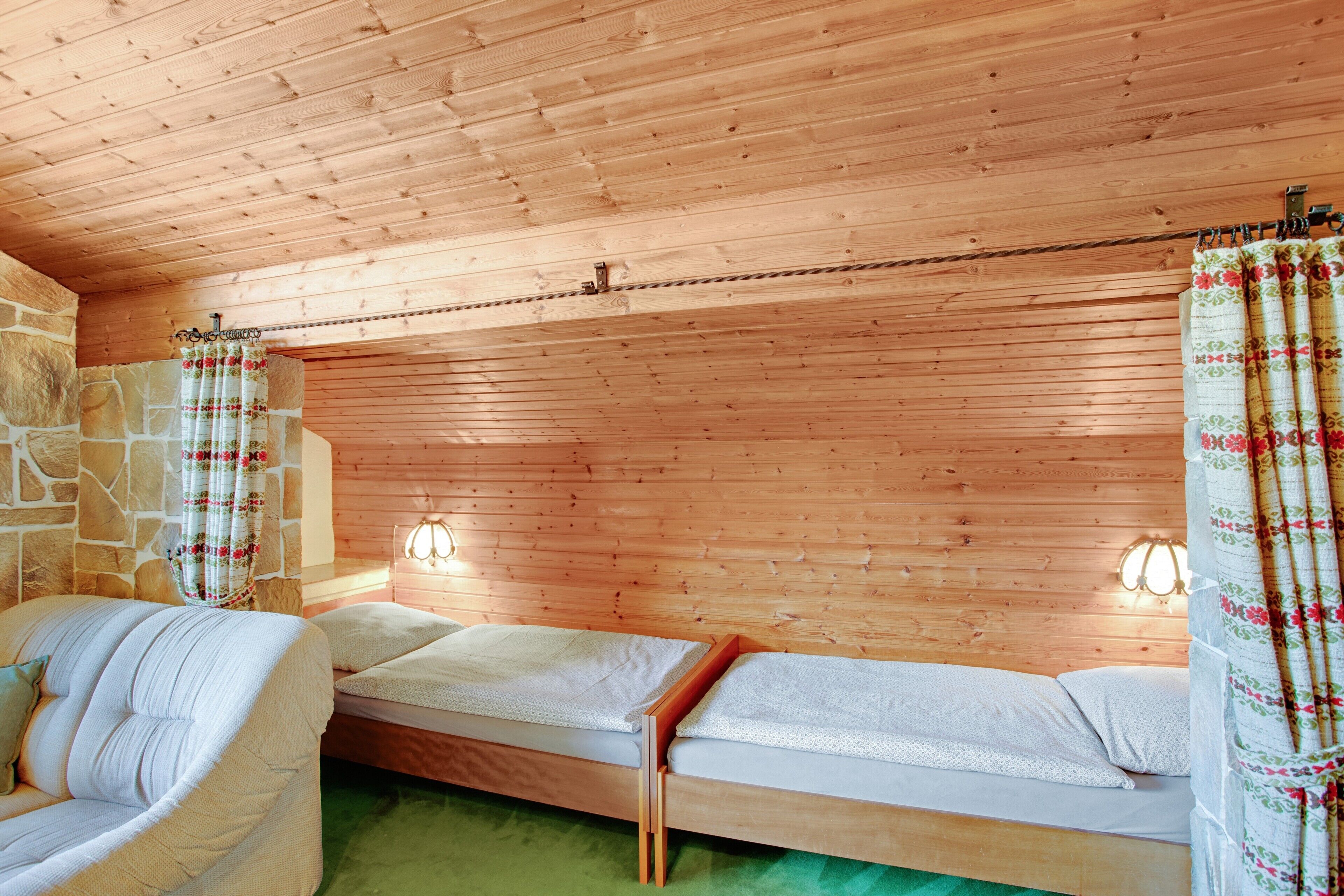Ein Zimmer mit Holzwänden, einer Steinwand, zwei Betten, einem Sofa und einem grünen Teppich.