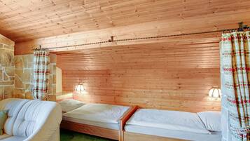 Ein Zimmer mit Holzwänden, einer Steinwand, zwei Betten, einem Sofa und einem grünen Teppich.