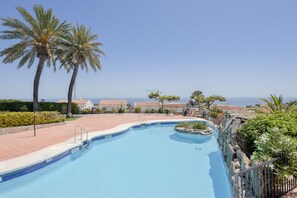 Une piscine avec vue sur la mer, des palmiers et un bâtiment avec un toit rouge.