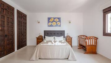 A bedroom with a bed, two nightstands, a crib, a wall-mounted painting, and wooden doors.