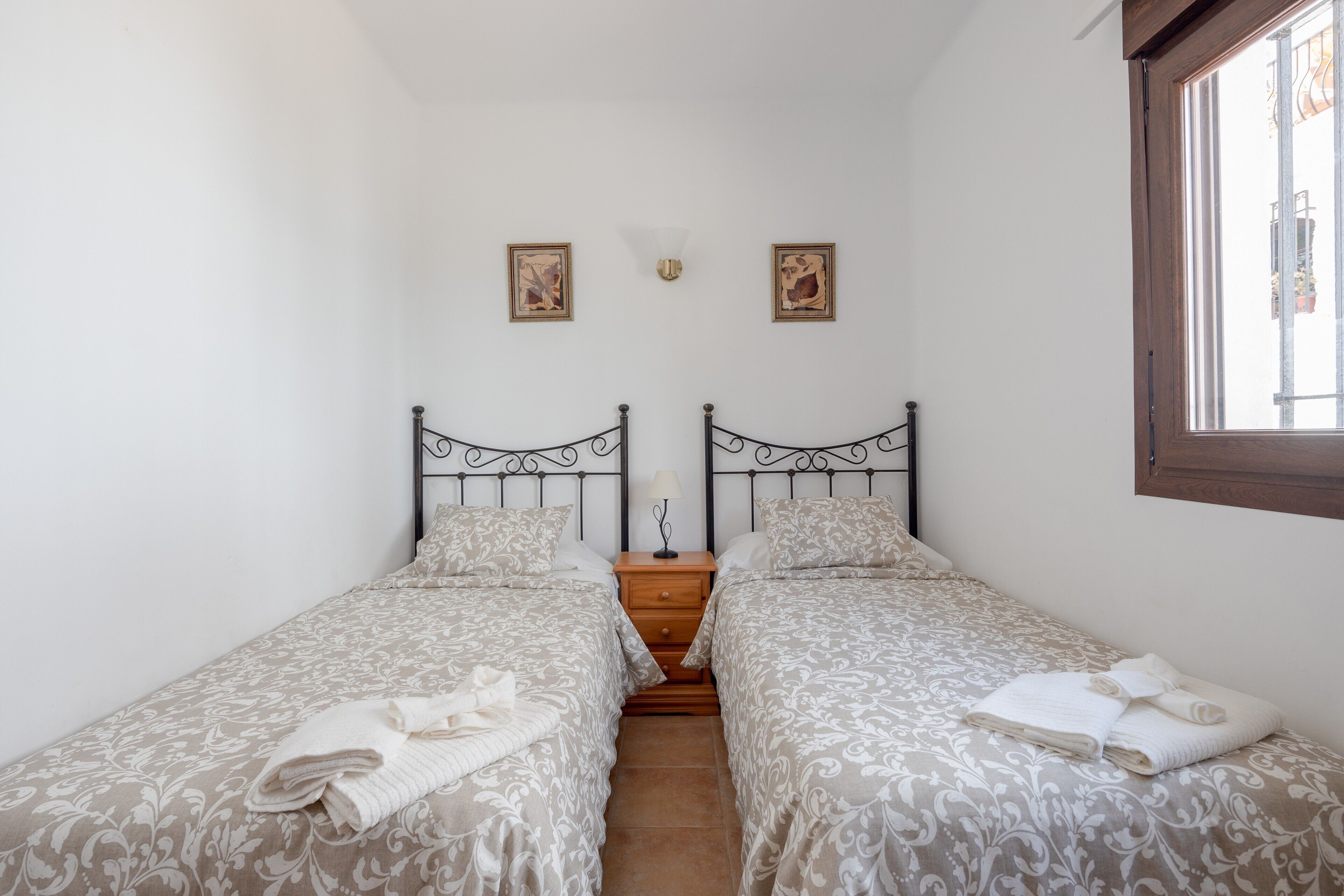 Un dormitorio doble con dos camas, una mesita de noche, una lámpara de pared y dos cuadros enmarcados.