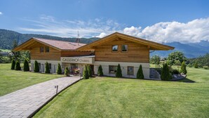 A two-story chalet with a sign reading 'GASSEROF Chalets,' a paved driveway, and a well-maintained lawn with coniferous trees. - Gasserhof - Chalet A with Balcony, Mountain View, Garden & Wi-Fi (Mölten)