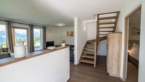 A modern interior with a wooden staircase, a kitchen area, and a view through large windows. - Gasserhof - Chalet A with Balcony, Mountain View, Garden & Wi-Fi (Mölten)